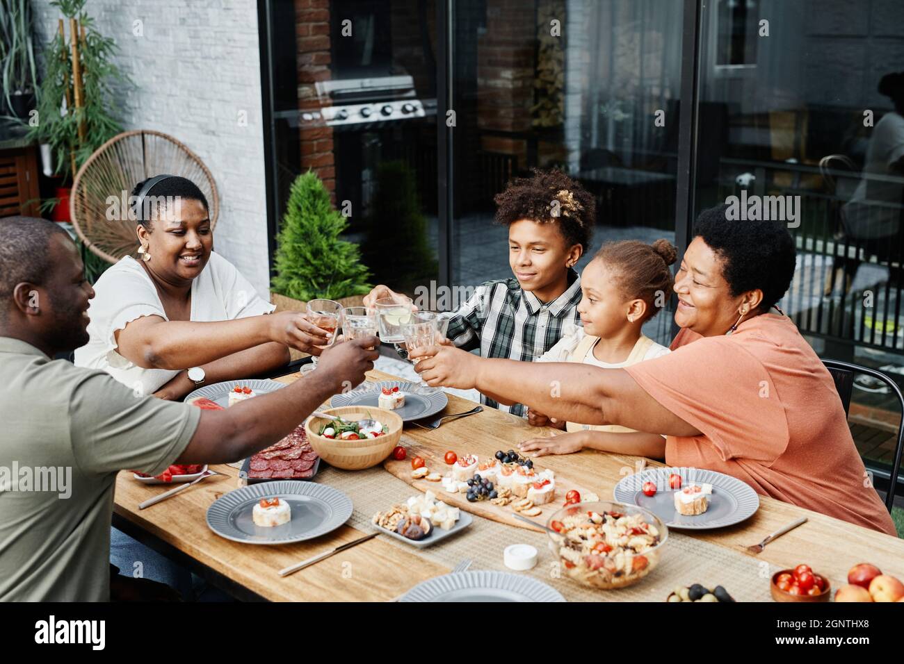Porträt großer afroamerikanischer Familiengläser, während sie gemeinsam im Freien essen und feiern Stockfoto