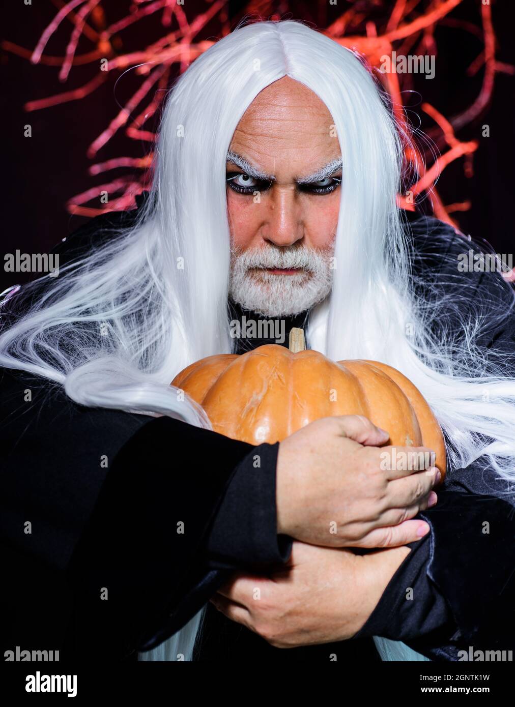 Teufelsmann mit Kürbis in der Hand. Bärtiger Mann im Hexenkostüm bereit zur Halloween-Party Stockfoto