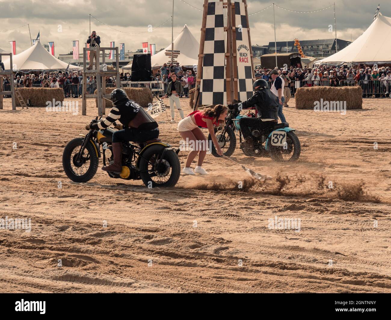 Ouistreham, Normandie, Frankreich, September 2021. STRANDRENNEN IN DER NORMANDIE. Junge Frau, die mit einer Startflagge springt, um das Signal zum Start für die Fahrer zu geben Stockfoto