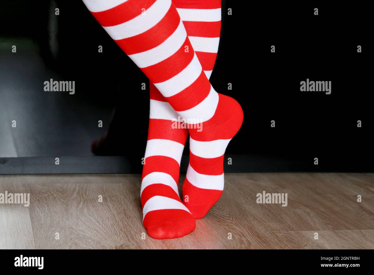 Weibliche Beine in Weihnachtskniesocken auf einem Boden auf schwarzem Kleiderschrank Hintergrund. Kleidung für Silvester Feier, Mädchen in Santa Kostüm Stockfoto