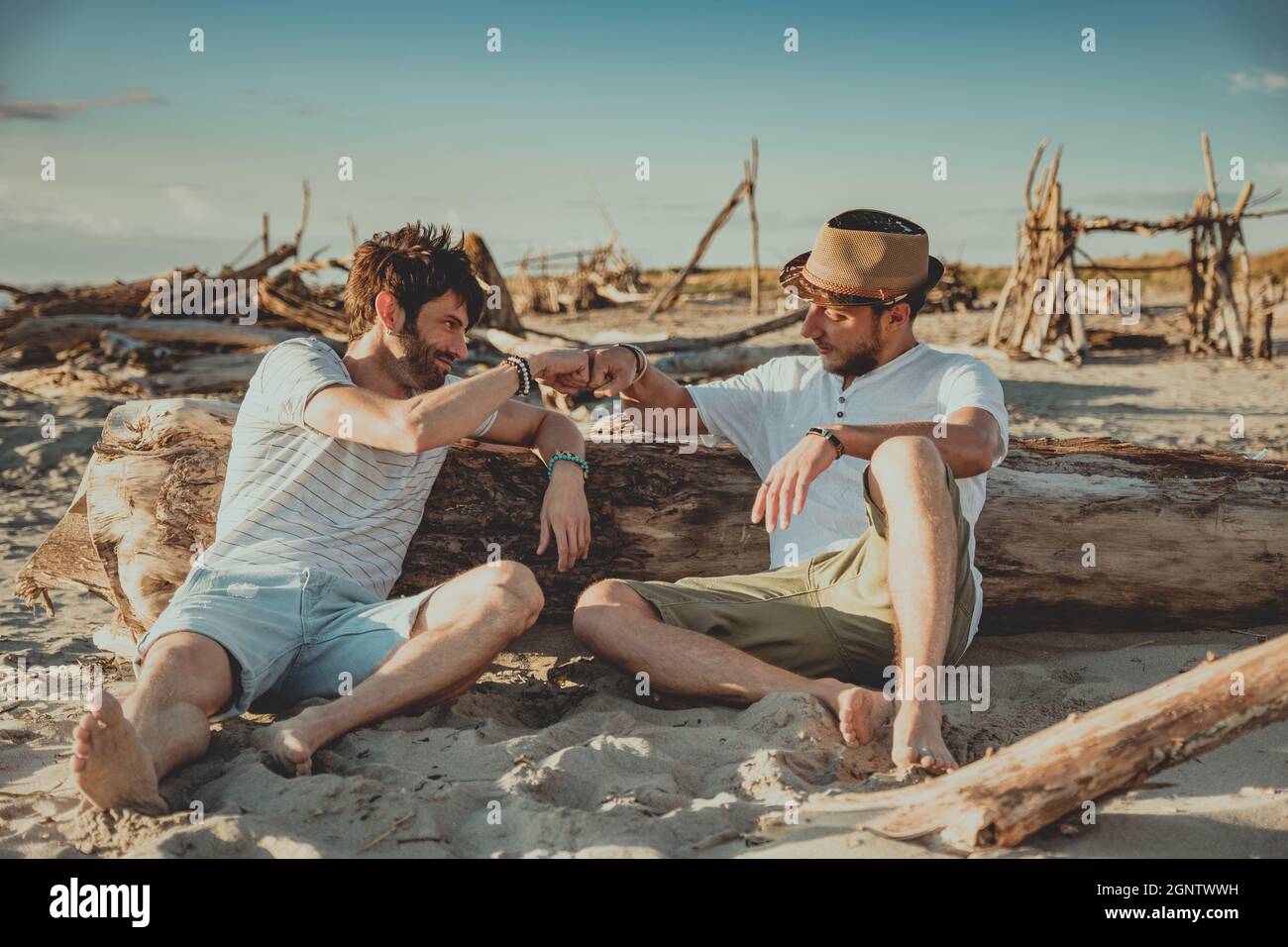 Zwei Jungen, die am Strand sitzen und sich mit ihren Fäusten begrüßen. Junge Menschen klopfen mit den Fäusten, um sich gegenseitig zu begrüßen Stockfoto