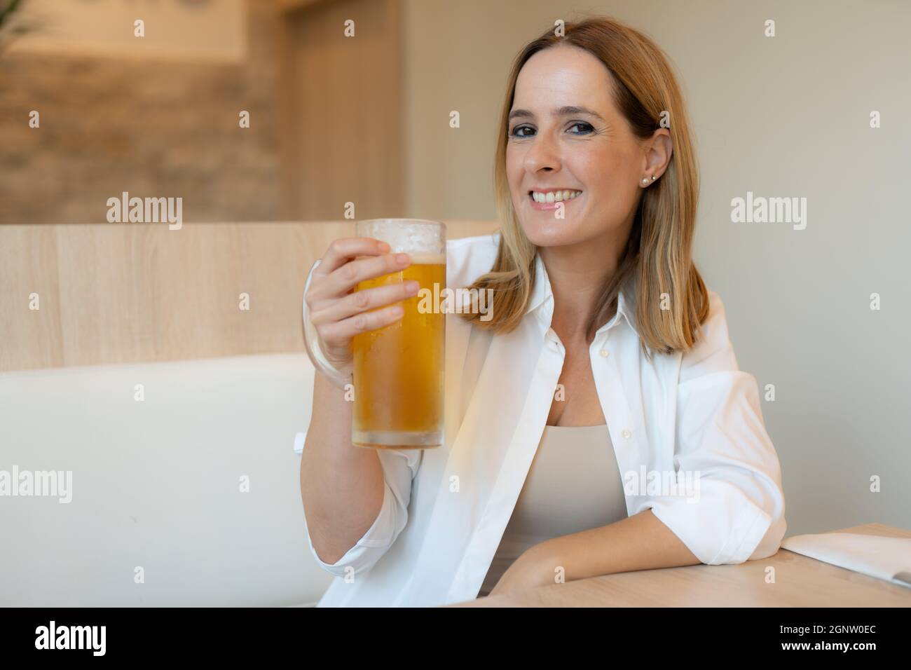 Junge lächelnde Frau, die in einem Restaurant ein Bier trinkt Stockfoto