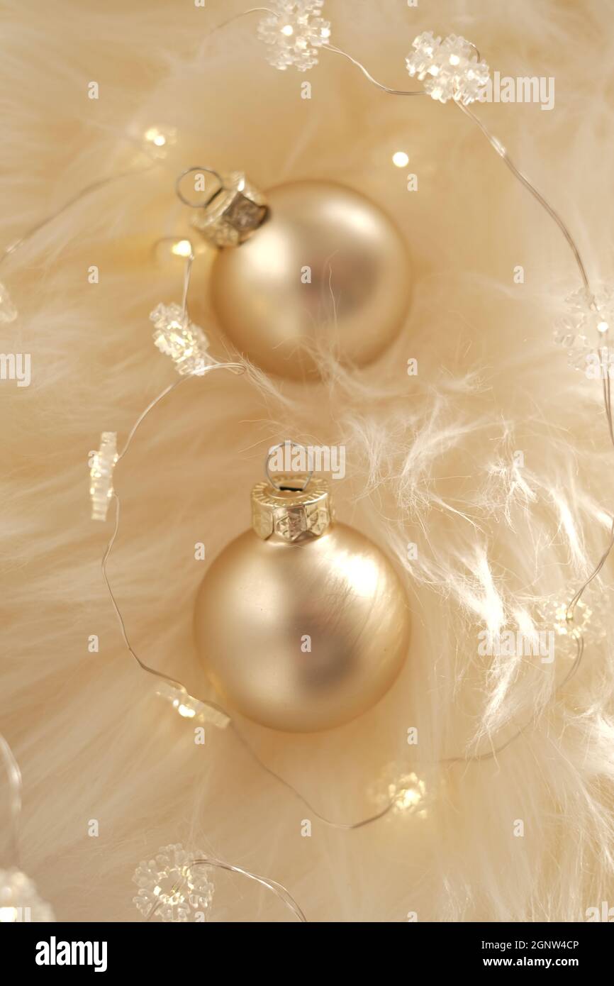 Weihnachtsdekor Kugeln.Weihnachtshintergrund mit glänzender Girlande und goldenen Kugeln auf beigem Fell in warmen Farben Stockfoto