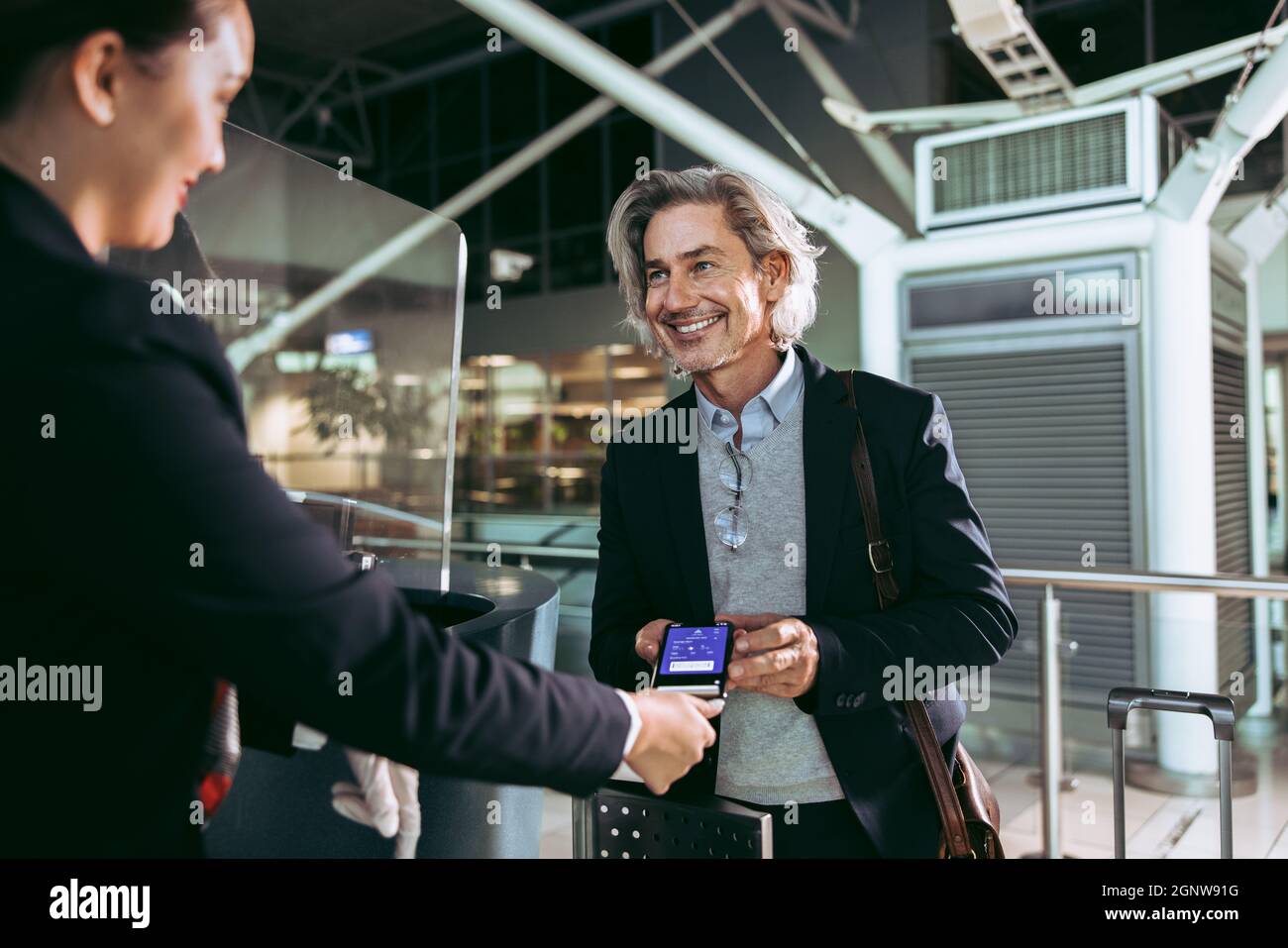Geschäftsmann zeigt dem Flugbegleiter am Check-in-Schalter am Flughafen die  elektronische Bordkarte. Lächelnder männlicher Reisender, der am Flughafen  einen digitalen Check-in macht Stockfotografie - Alamy