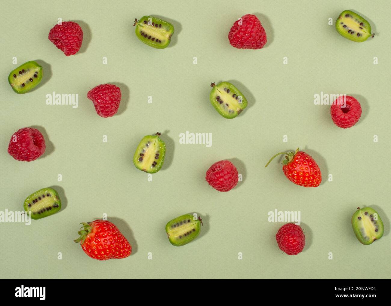 Frucht der Actinidia arguta, Kiwi-Beerenfrüchte und Himbeeren auf grünem Hintergrund. Stockfoto