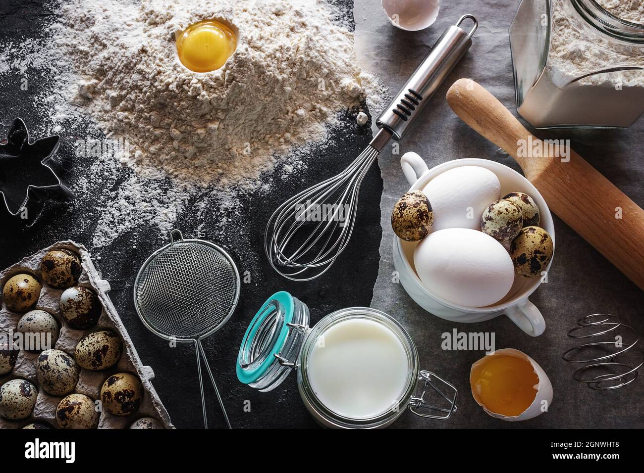 Backwaren und Utensilien auf schwarzem Hintergrund, Milch, Eier, Mehl Stockfoto