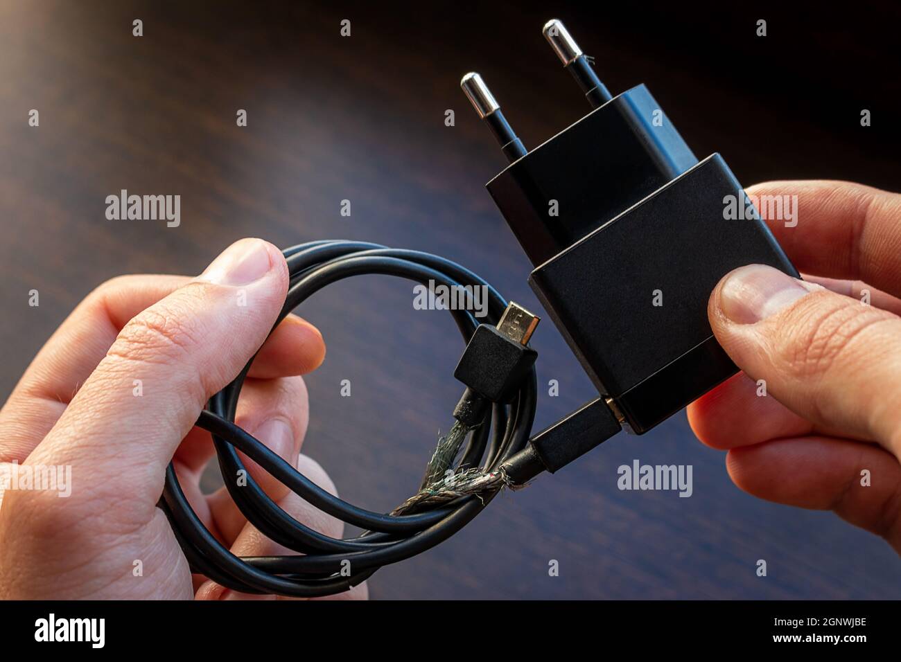 Halten Sie ein altes, defektes Smartphone-Ladegerät mit blanken Kabeln in der Nähe Stockfoto