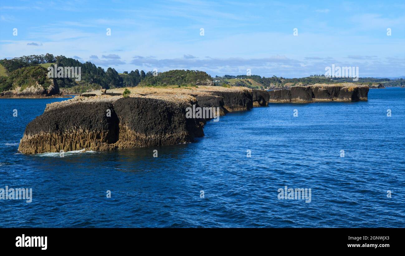 The Black Rocks, eine Gruppe kleiner Inseln aus uralter Basaltlava in der Bay of Islands, Neuseeland. Im Hintergrund ist die Insel Moturoa Stockfoto