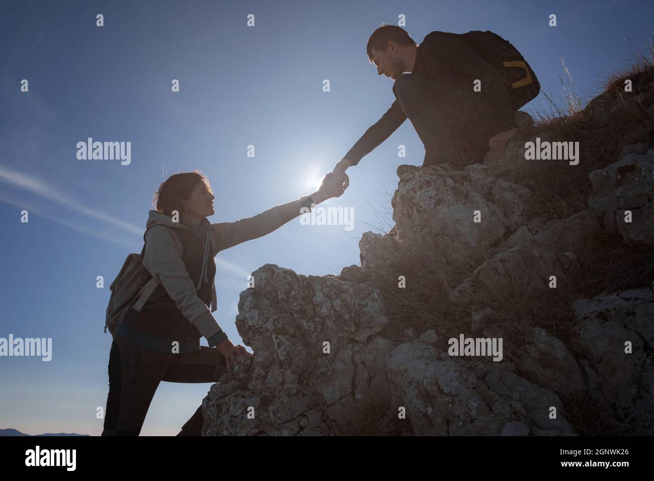 Hilfe- und Hilfekonzept. Silhouetten von zwei Menschen, die Berge besteigen und gegen den blauen Himmel helfen. Gehen Sie in den Wolken. Discovery Travel Direc Stockfoto