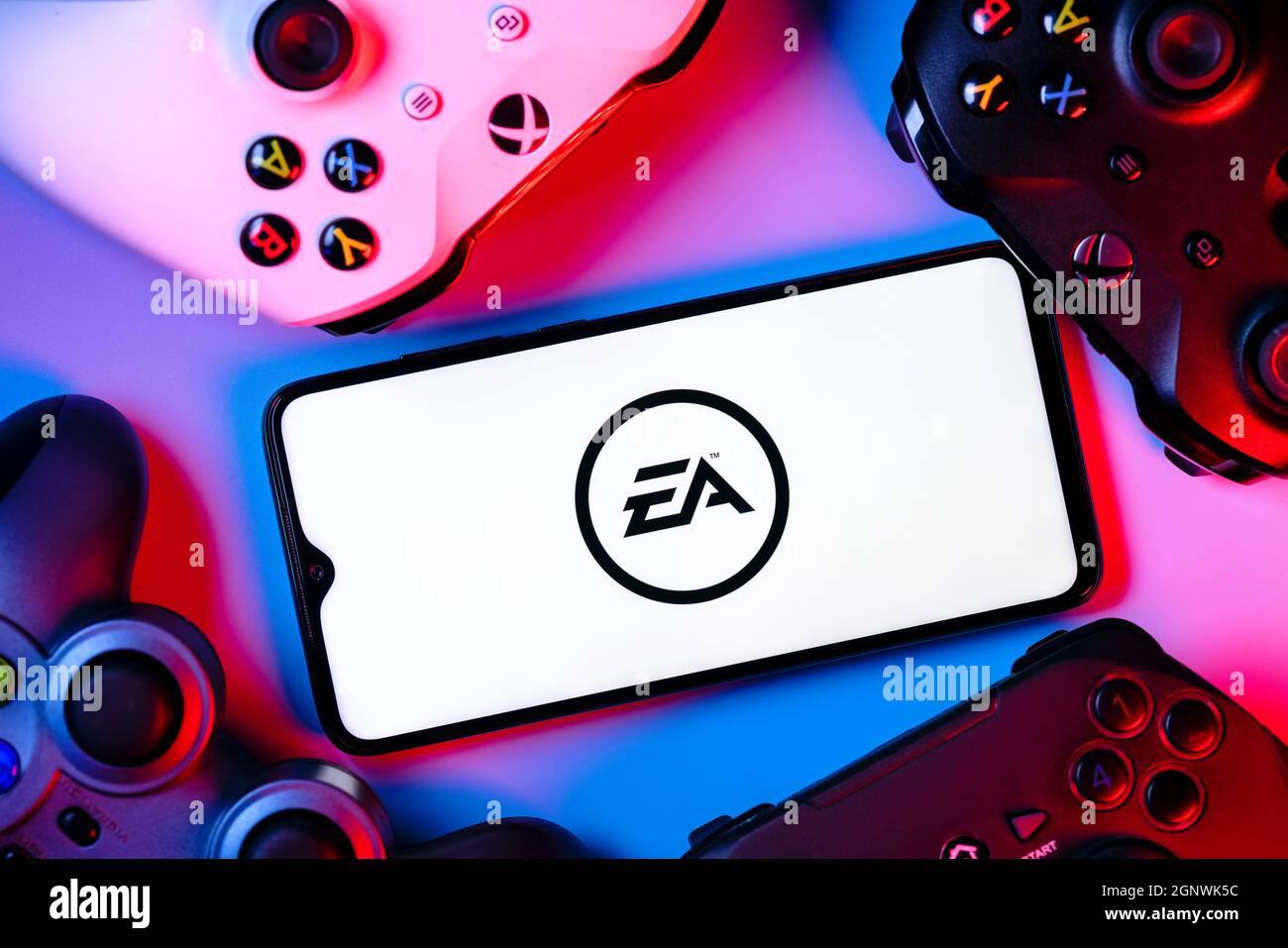 Ein Smartphone mit dem Electronic Arts-Logo auf dem Bildschirm, umgeben von Gamepads. Stockfoto