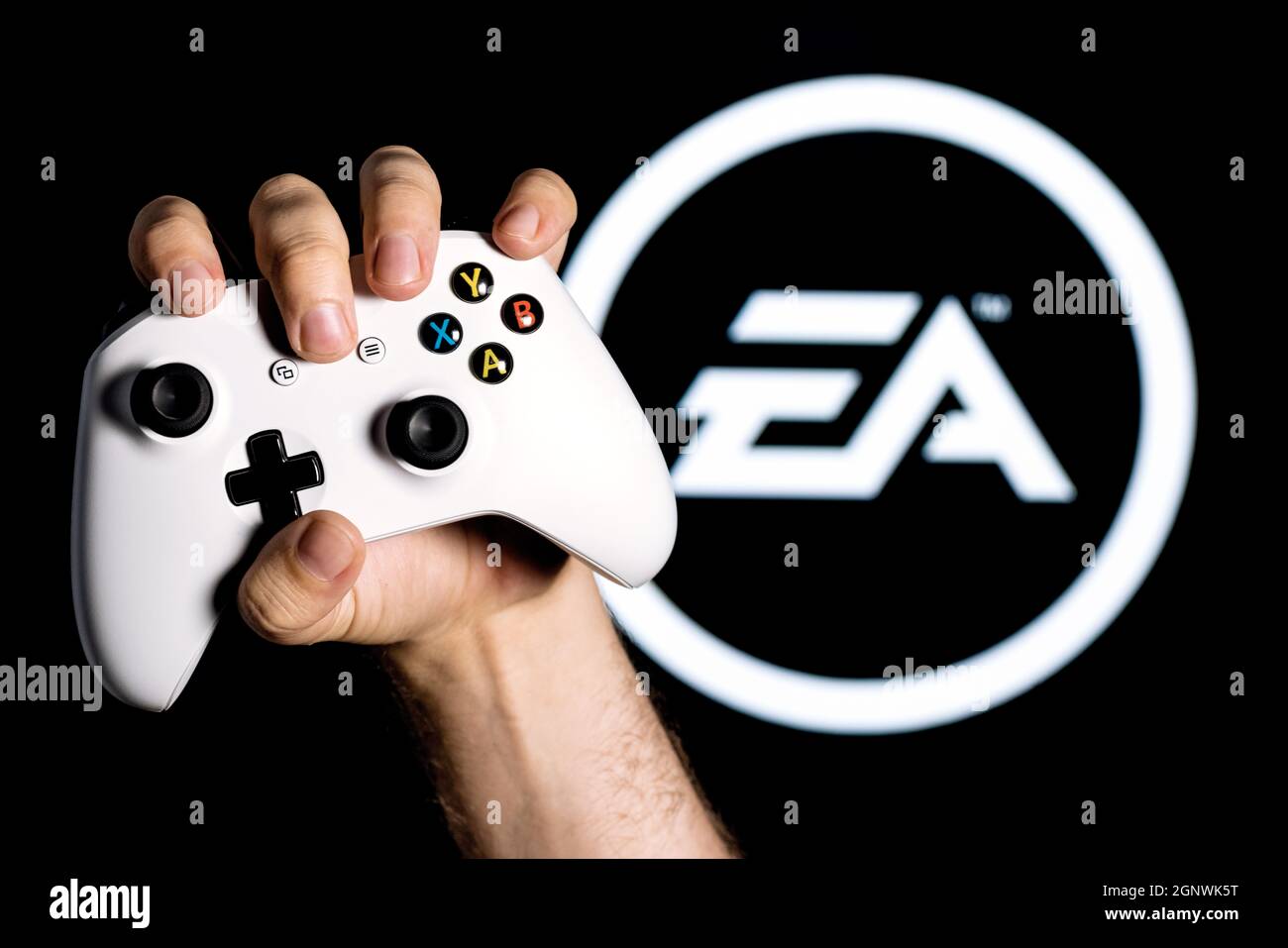 Ein weißer Gamepad in der Hand auf dem schwarzen Hintergrund mit dem Logo der Electronic Arts geklammert Stockfoto