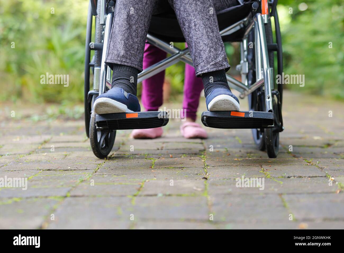 Ältere Frau im Rollstuhl, die mit der Pflegekraft läuft Stockfoto