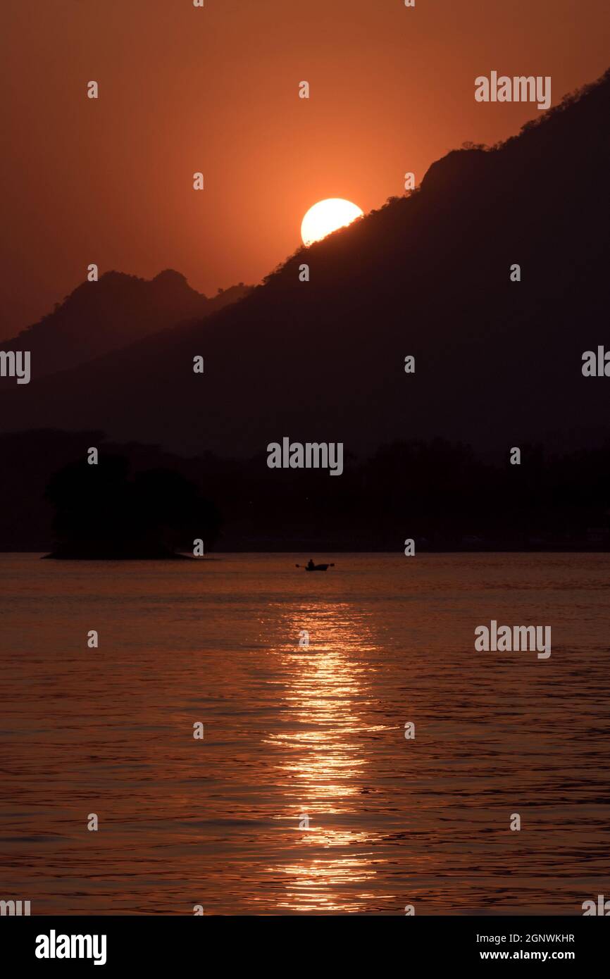 Epische Landschaftsaufnahme des Sonnenuntergangs hinter den Bergen am See Fateh Sagar in Udaipur, Rajasthan Stockfoto