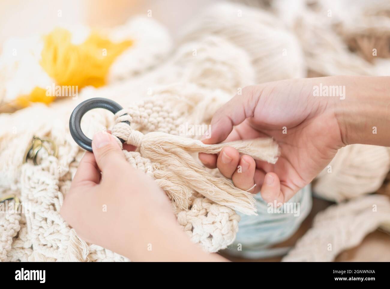 Weibliche Hände, die Hand aus Macrame beige Faden Hänge mit Holz hängen für die Überprüfung des Details und das perfekte Produkt. Es ist ein Handwerk zum Entspannen Stockfoto