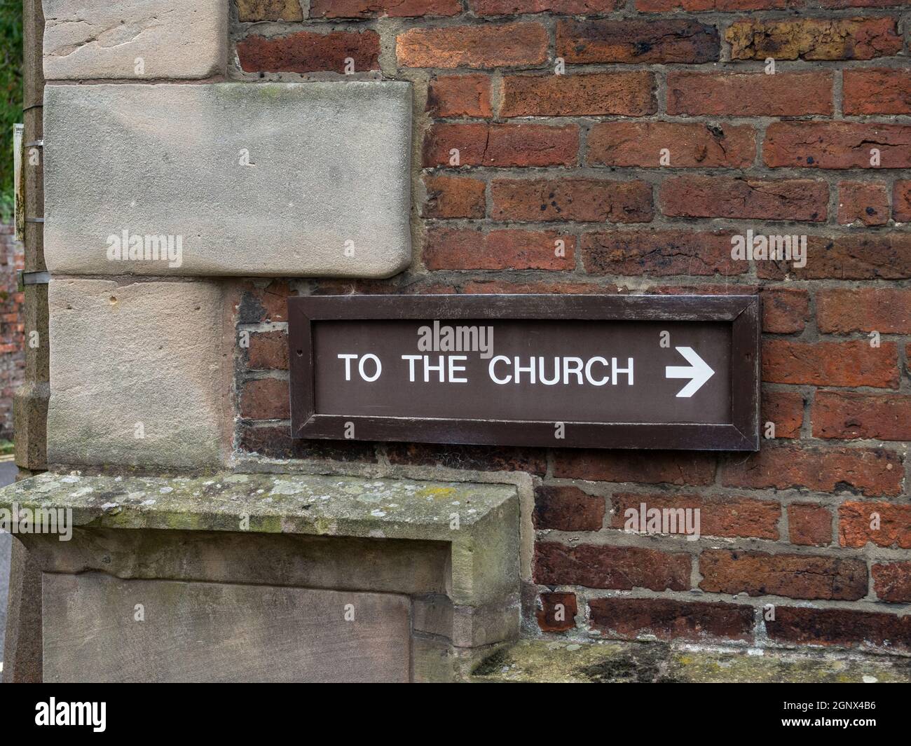 Zur Kirche altes Holzschild an einer alten Backsteinmauer, St. Oswald Kirche, Ashbourne, Derbyshire, Großbritannien Stockfoto