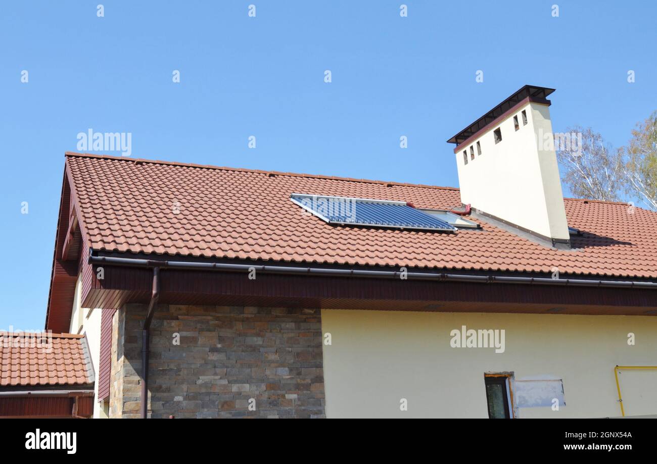Solarwarmwasserbereiter auf dem modernen Hausdach mit Dachfenster, Dachrinne und Kamin Stockfoto