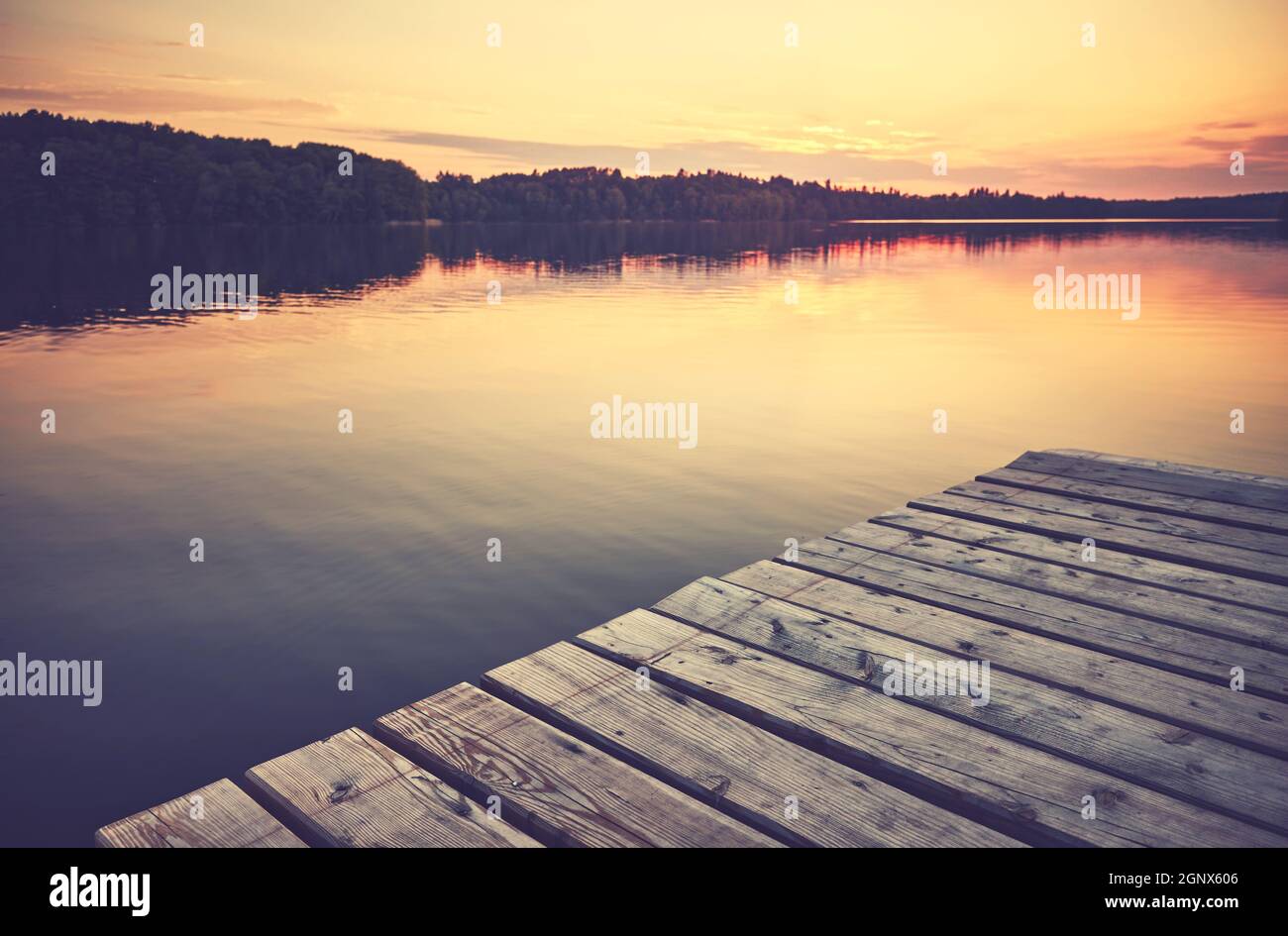 Sonnenuntergang über stillem See, Holzsteg im Vordergrund, Farbtonung aufgetragen. Stockfoto