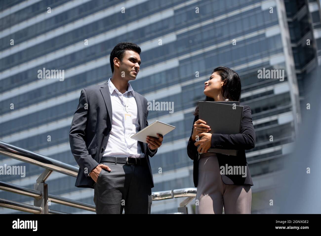 Hübscher junger indischer Geschäftsmann in Firmenkleidung im Gespräch mit einer Geschäftsfrau im Freien in der Stadt Stockfoto