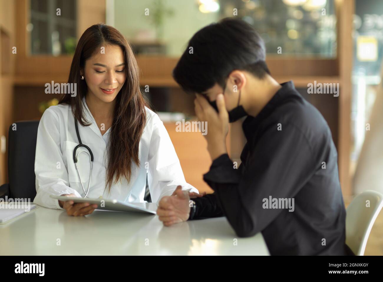 Schöne junge asiatische Ärztin ermutigt und erklärt einem männlichen Patienten den Operationsplan. Stockfoto