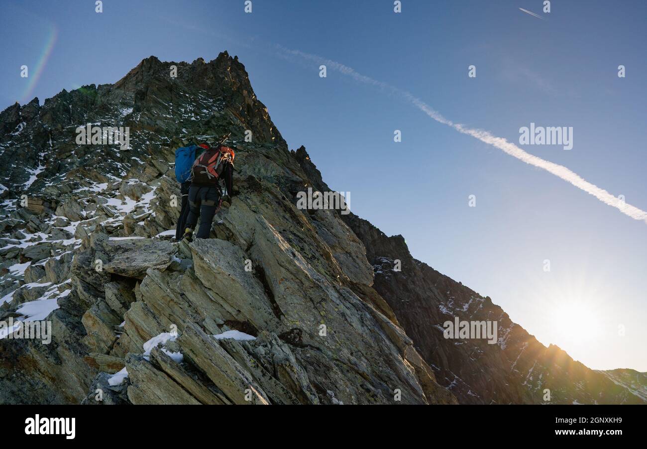 Rückansicht von Felskletterern mit Rucksäcken mit festem Seil beim Aufstieg auf einen hohen felsigen Berg. Männliche Bergsteiger klettern auf natürliche Felsformationen Stockfoto