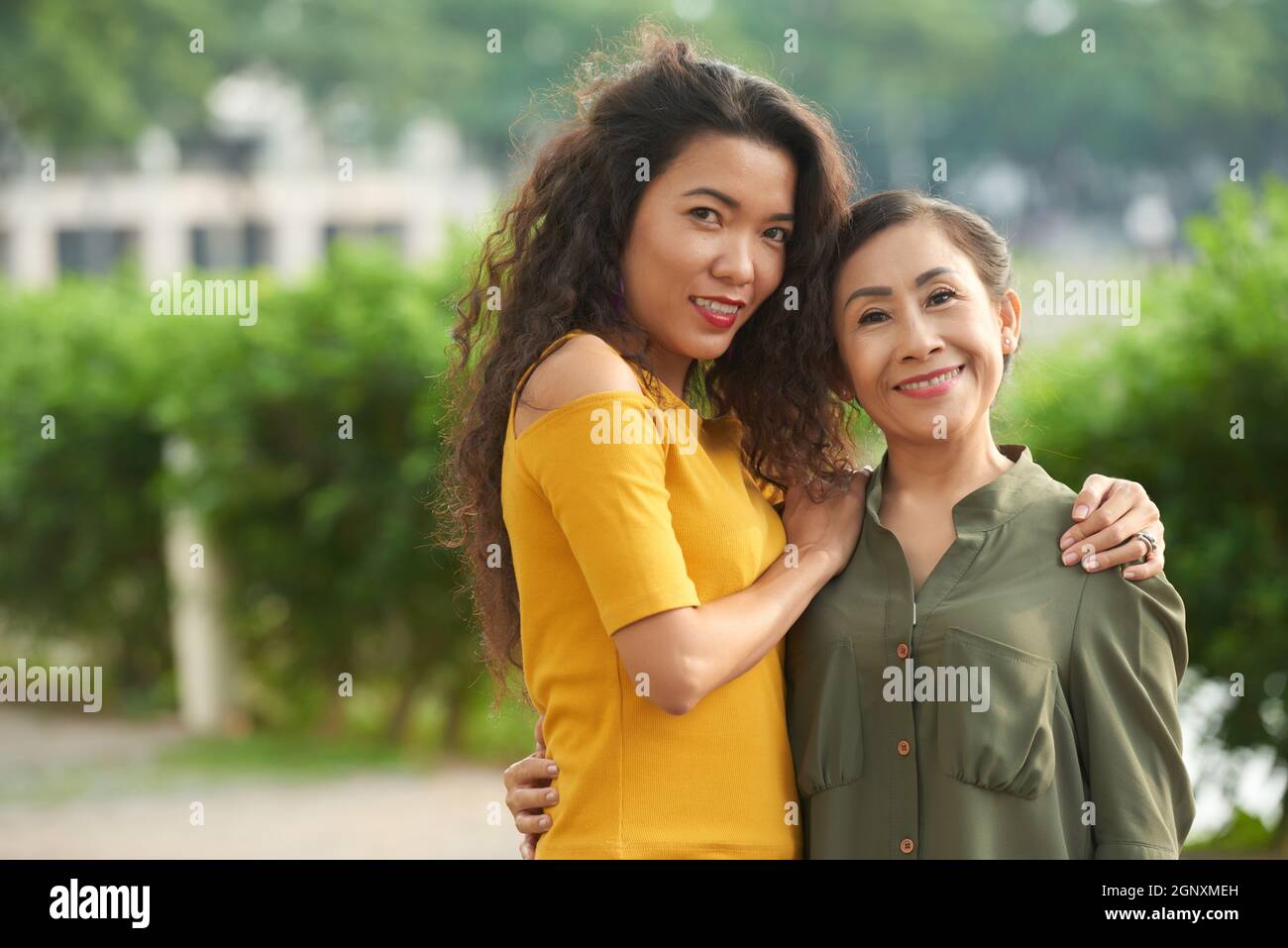 Portrait einer positiven erwachsenen vietnamesischen Tochter, die reife Mutter auf der Straße umarmt Stockfoto