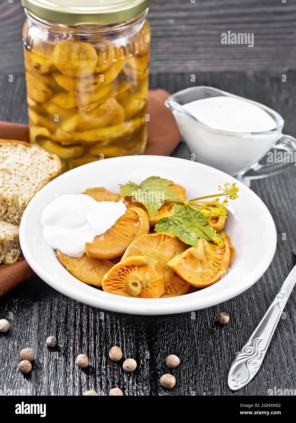 Gesalzene Pilze Safran mit saurer Sahne, Johannisbeerblatt und Zweig Dill in Teller, Gabel, Serviette und Brot auf dem Hintergrund von Holzbrett Stockfoto