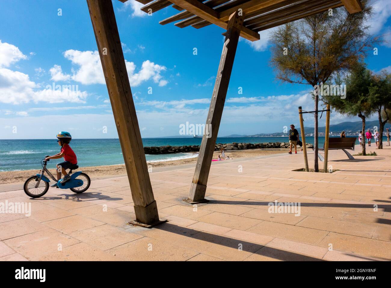 Ein Kind, das auf einem Radweg an der Strandpromenade Paseo Maritimo El Molinar, Palma de Mallorca Spanien fährt, pflasterte einen öffentlichen Spaziergang entlang des Kleinkindes am Meer Stockfoto