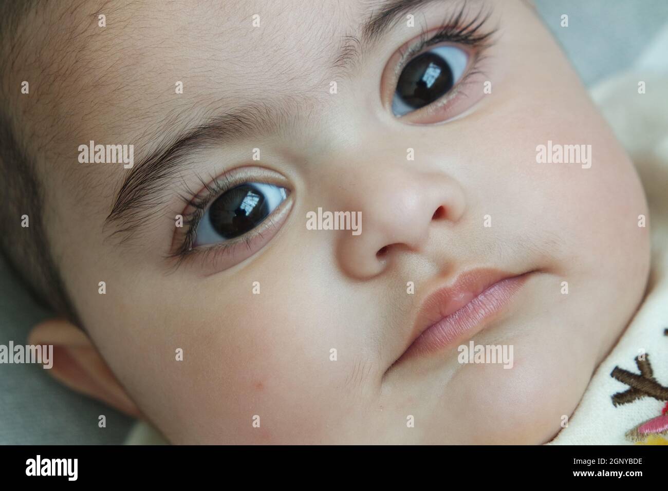 Baby Mädchen mit schwarzen Augen starrte auf die Kamera. Baby mit schönem Gesicht, großen Augen und niedlichen Gesichtsgesten. Stockfoto