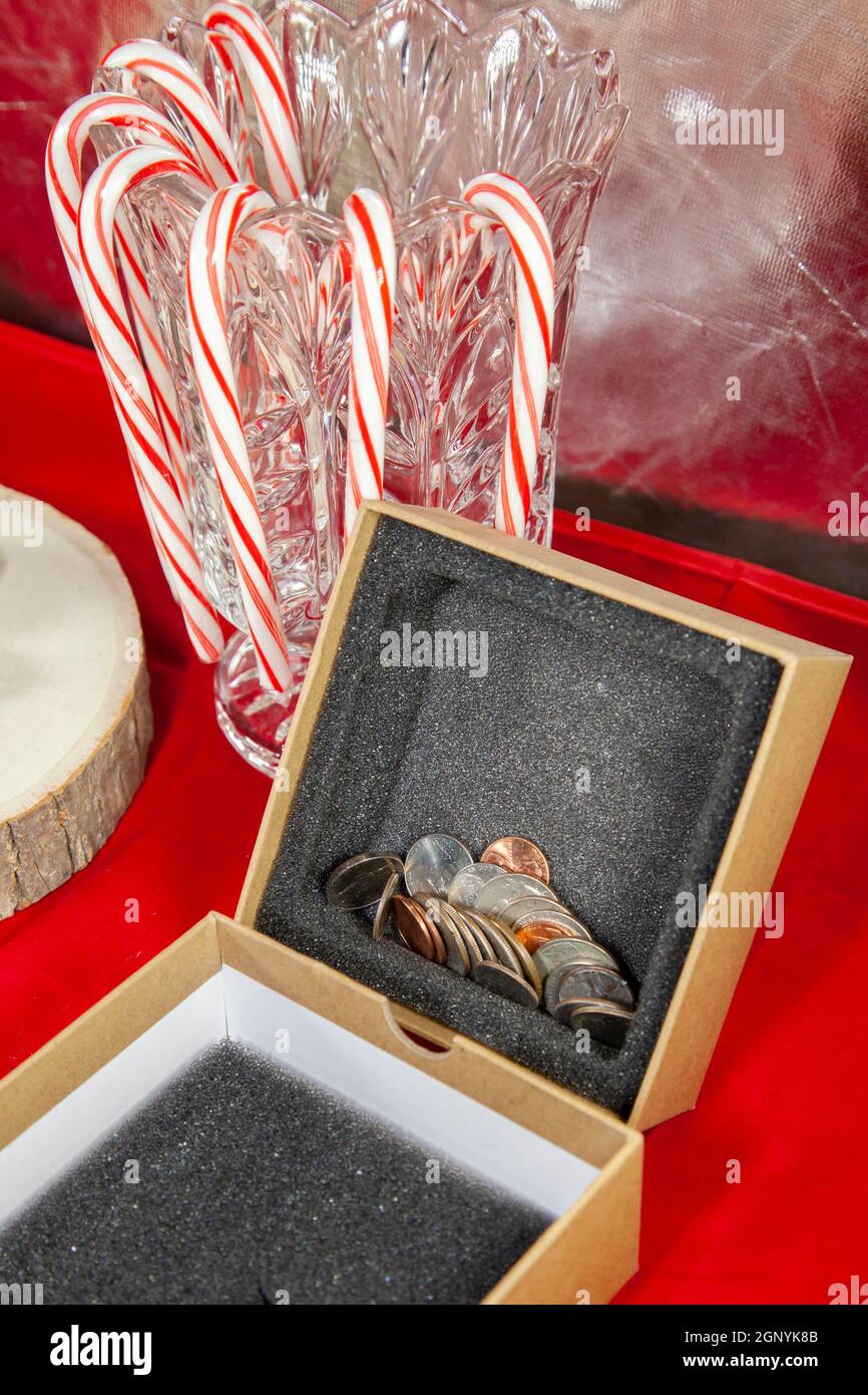 Leere, unverpackte Geschenkschachtel, gefüllt mit Pennies, Nickels, Dimes, Quarters und einer Dollarmünze, auf einer roten Tischplatte mit Zuckerstöcken im Hintergrund Stockfoto