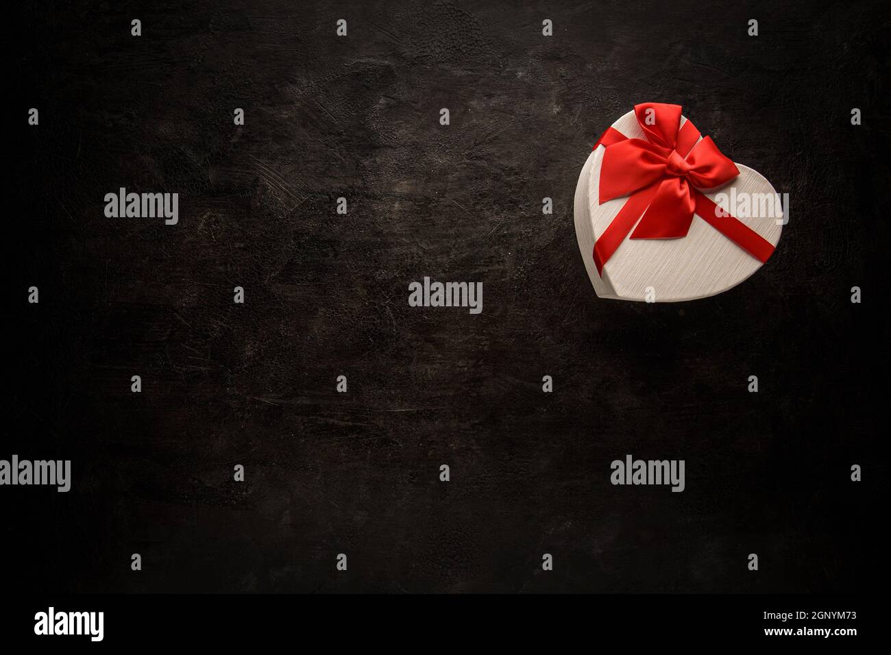 Geschenkbox mit einem roten Band herzförmig mit leerem Raum Für Text auf schwarzem Hintergrund Stockfoto