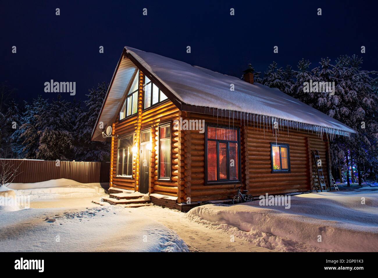 Rustikales Blockhaus, schneebedeckte Pinien, Schneeverwehungen, fabelhafte Winternacht. Ländliche schöne Winterlandschaft. Mieten Sie suburbanes Gehäuse, Immobilien Stockfoto