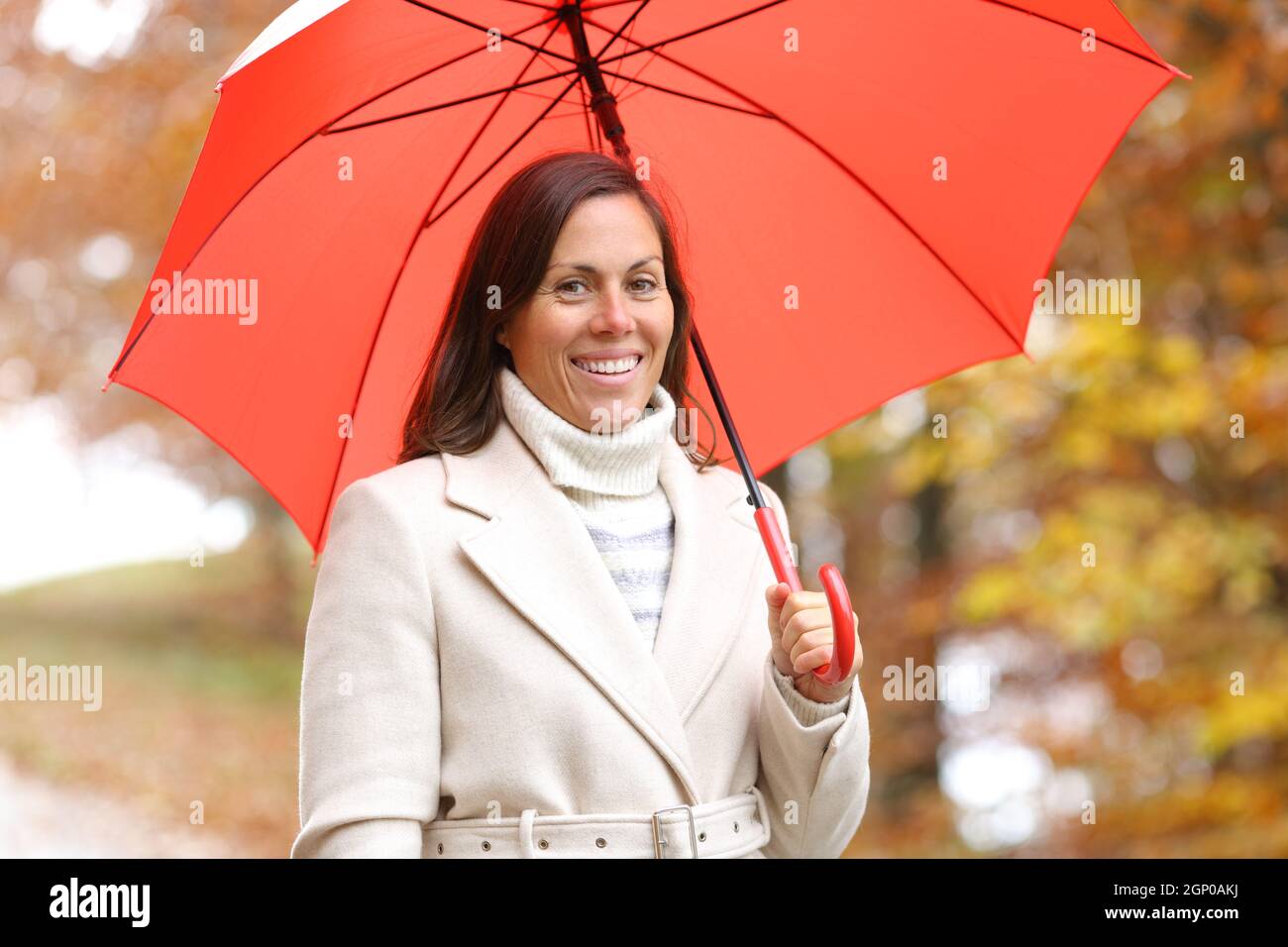 Glückliche Frau posiert Blick auf Kamera im Winter mit Regenschirm In einem Park Stockfoto