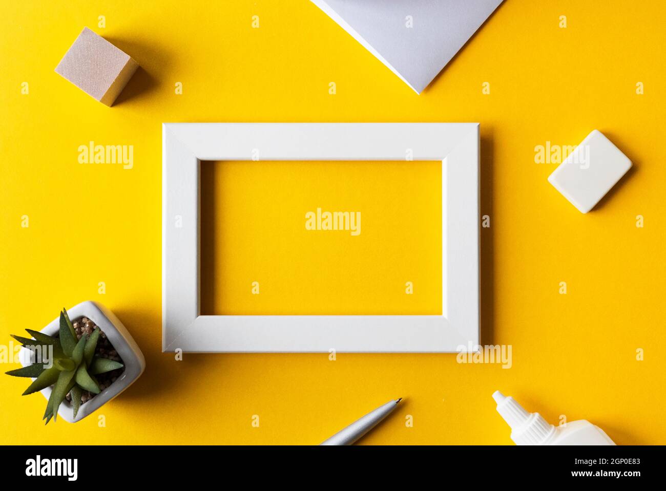 Kreativer Arbeitsplatz oder Arbeitsplatz mit hellgelber Oberfläche, leerem Fotorahmen, Bürozubehör, Draufsicht, Platz für Text. Stockfoto
