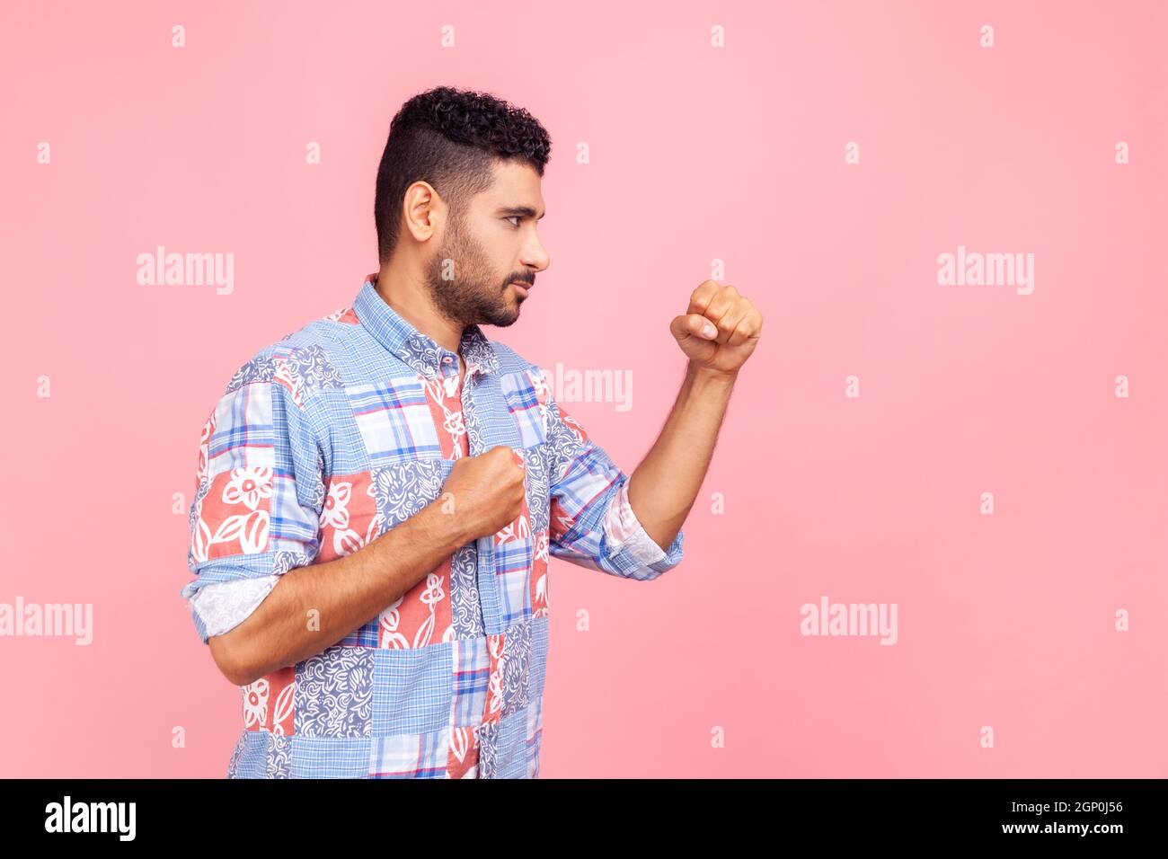 Profilportrait eines aggressiven jungen erwachsenen Mannes in blauem Hemd, der mit Boxfäusten steht und bereit ist, anzugreifen oder zu verteidigen, und mit einem wütenden Gesicht aussieht. Innenaufnahme des Studios isoliert auf rosa Hintergrund. Stockfoto