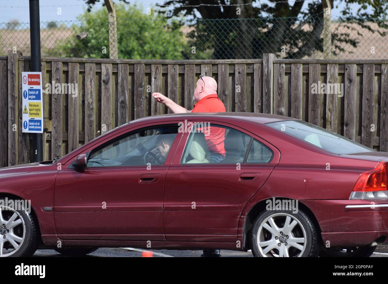 Ein wütender Mann, der an einer Tankstelle in Großbritannien nach Kraftstoff Schlange steht, verliert seine Geduld, verlässt sein Auto und schreit wütend auf ein bereits füllendes Auto Stockfoto
