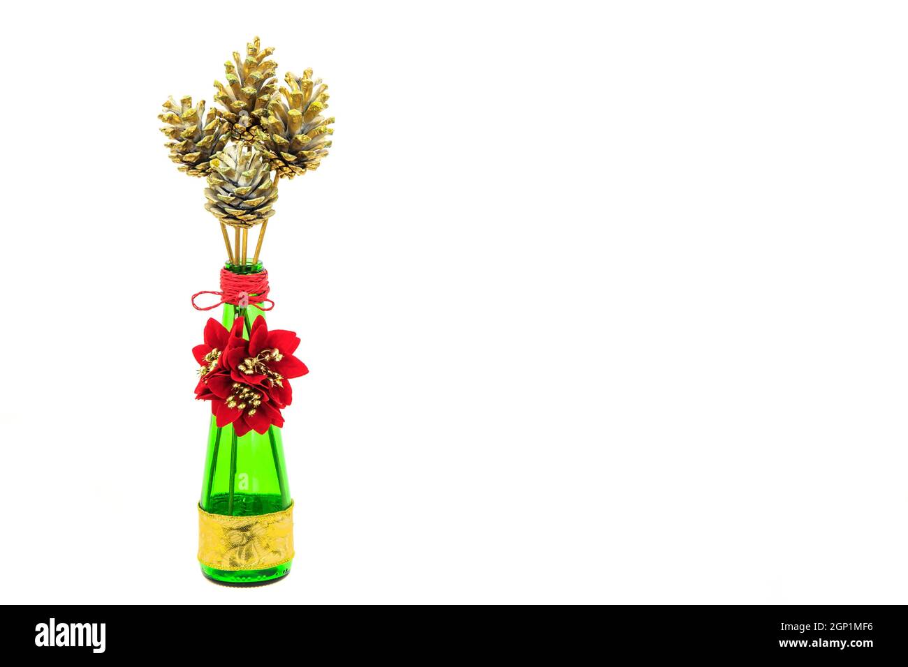 Goldbemalte Tannenzapfen und Poinsettienblüten in einer grünen Flasche isoliert auf Weiß Stockfoto