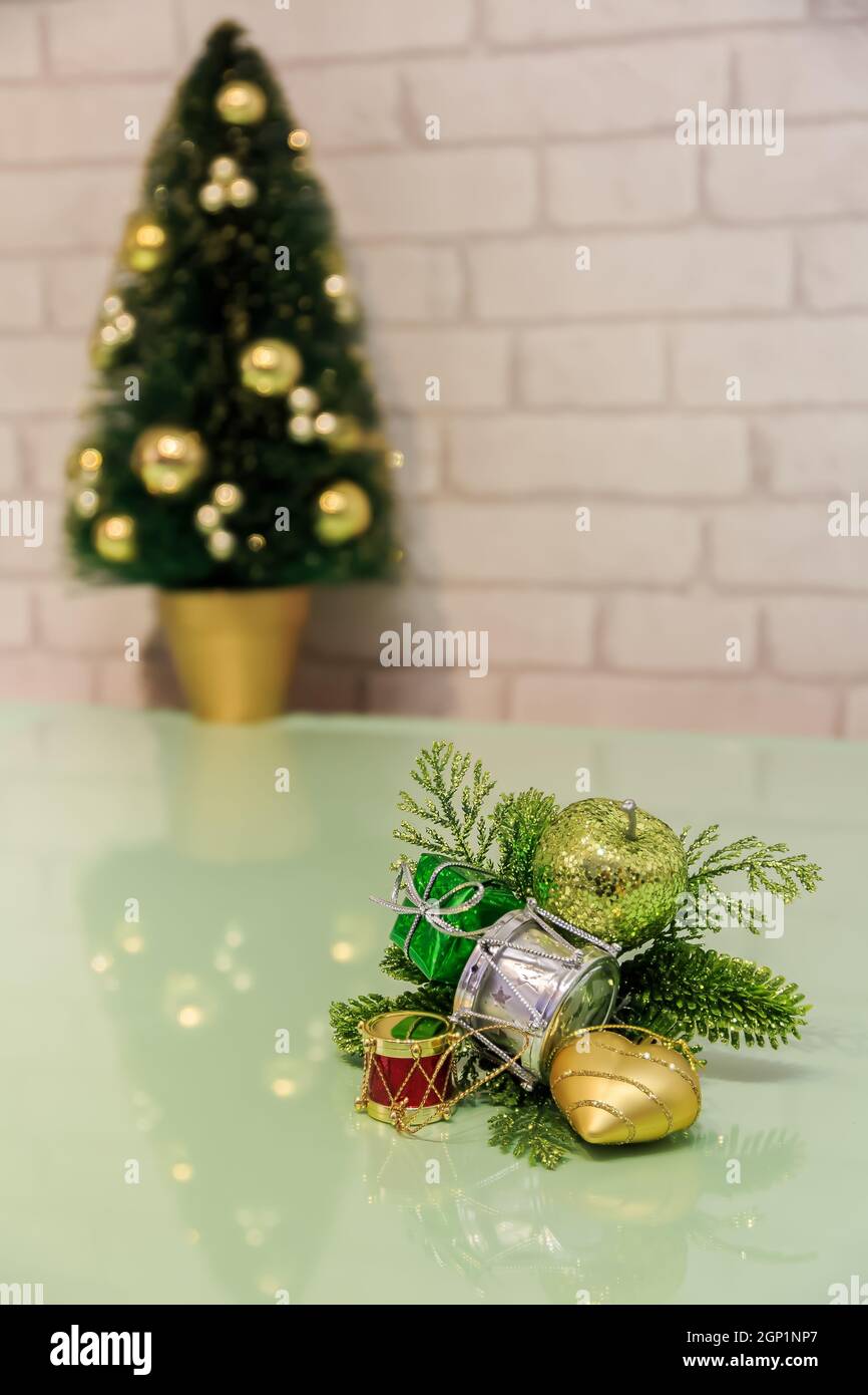 Weihnachtsdekoration mit Spiegelung auf einer grünen Arbeitsplatte und verschwommenem Weihnachtsbaum mit Lichtern im Hintergrund Stockfoto