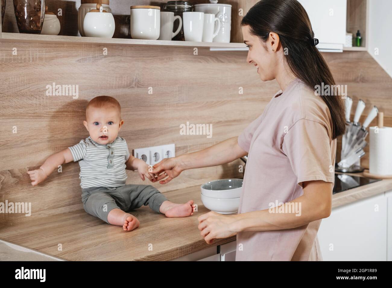 Beschäftigt Mutter Reinigung Küche mit Baby auf den Armen. Frau kocht und hält Säugling, müde Frau macht tägliche Hausaufgaben mit Kind. Stockfoto