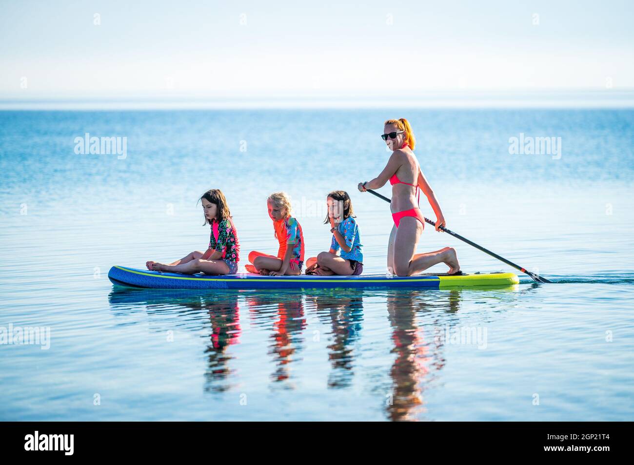 Glückliche Familie auf SUP Stand Up Paddle im Urlaub. Aktive Familie auf SUP-Boards reiten und an einem schönen Morgen im Meer paddeln. Mutter und drei gi Stockfoto