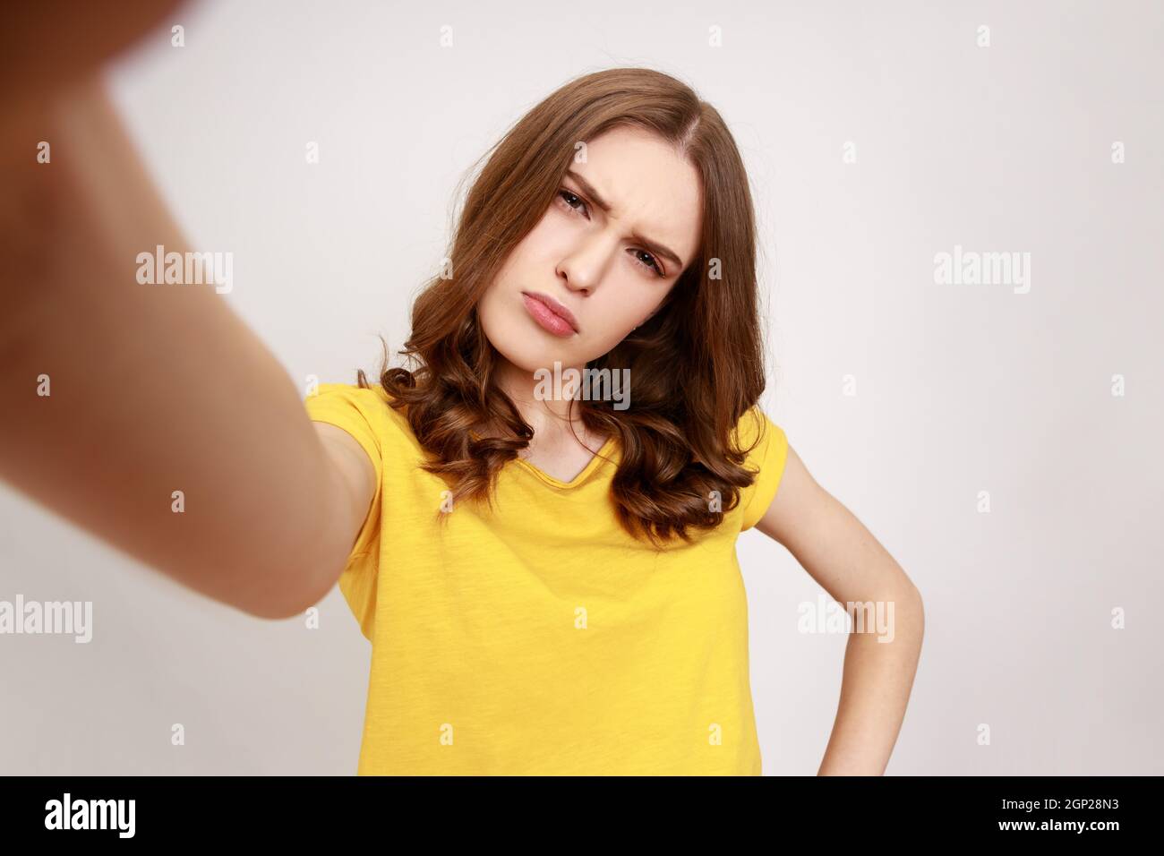 Verwirrt schönes Teenager-Mädchen in gelbem legerem T-Shirt, das auf den POV der Kamera schaut, Standpunkt des Fotos, Stirnrunzeln, missverständlicher Ausdruck. Innenaufnahme des Studios isoliert auf grauem Hintergrund. Stockfoto