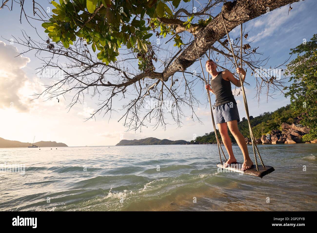 Schöner sonniger Tag am Strand. Glücklicher Mann auf Schaukel, der den Urlaub auf den Seychellen genießt. Stockfoto