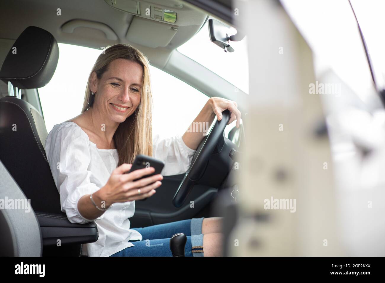 Hübsche Frau mittleren Alters mit am Steuer ihres Autos, mit einem Smartphone Stockfoto