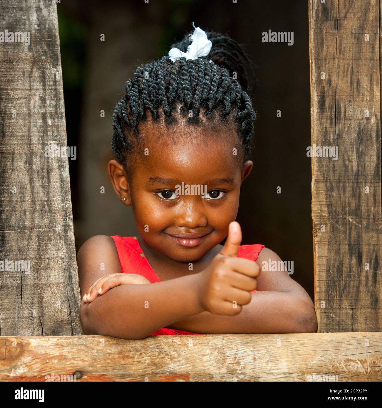 Portrait eines kleinen afrikanischen Mädchens, das Daumen nach oben am Holzzaun tut. Stockfoto
