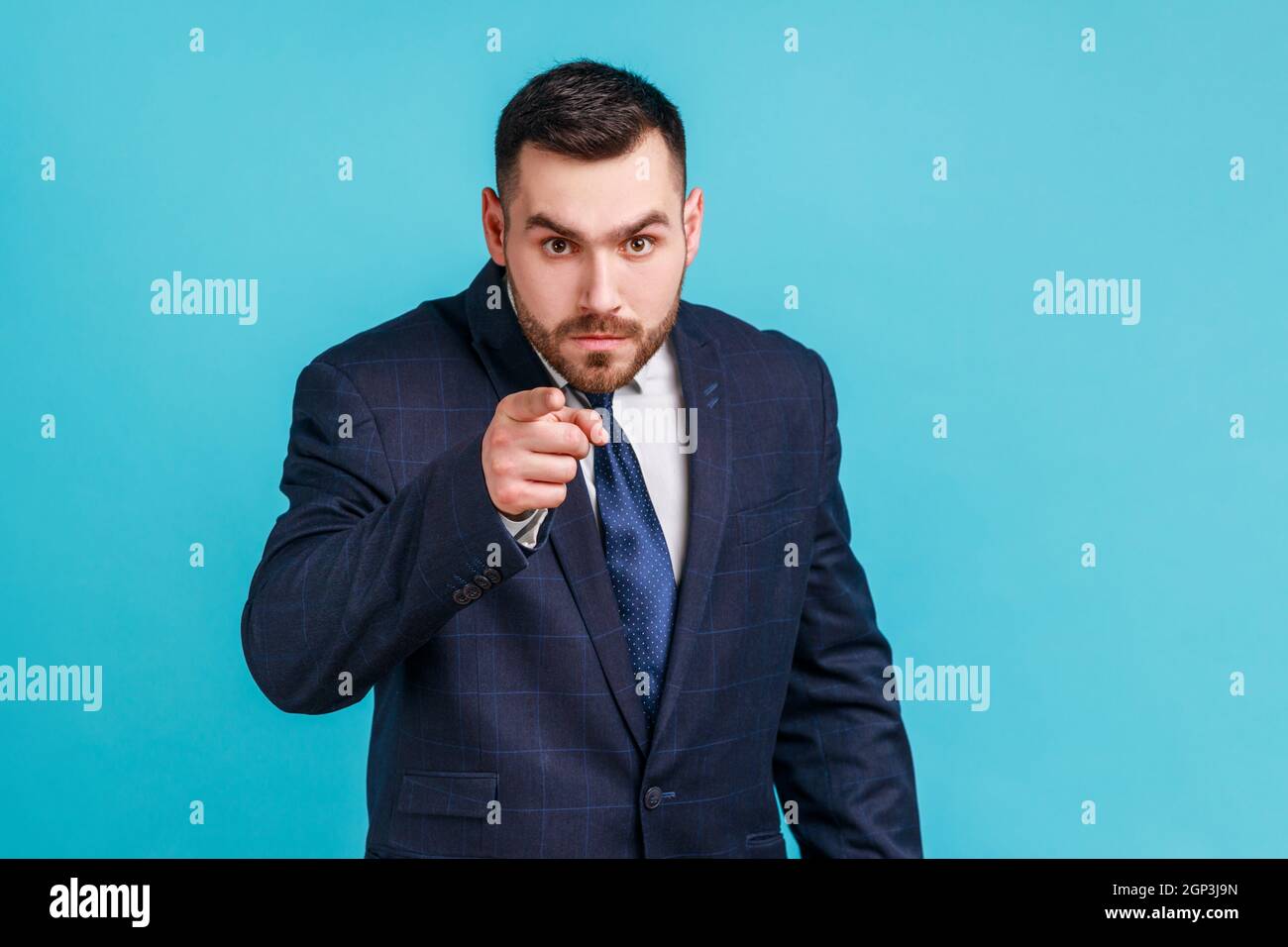 Ernsthafter bärtiger Mann mit offiziellem Anzug, der mit dem Finger zeigt, die Richtung zur Kamera anzeigt und verärgert aussieht und die Wahl getroffen hat. Innenaufnahme des Studios isoliert auf blauem Hintergrund. Stockfoto