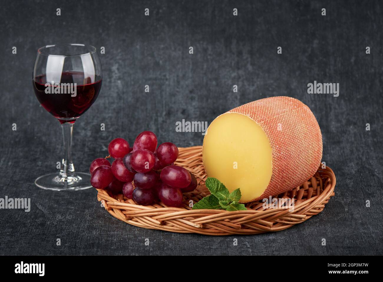 Köstlicher Tete de moine Käse in einem flachen Korb mit Weinrebe neben einem Glas Wein. Traditioneller Schweizer Käse Stockfoto