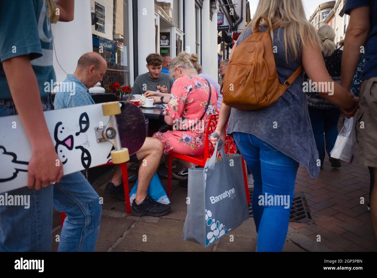 Schräge Straßenaufnahme einer älteren Familie, die draußen auf einem Café-Straßentisch mit vorbeiziehenden Leuten isst Stockfoto