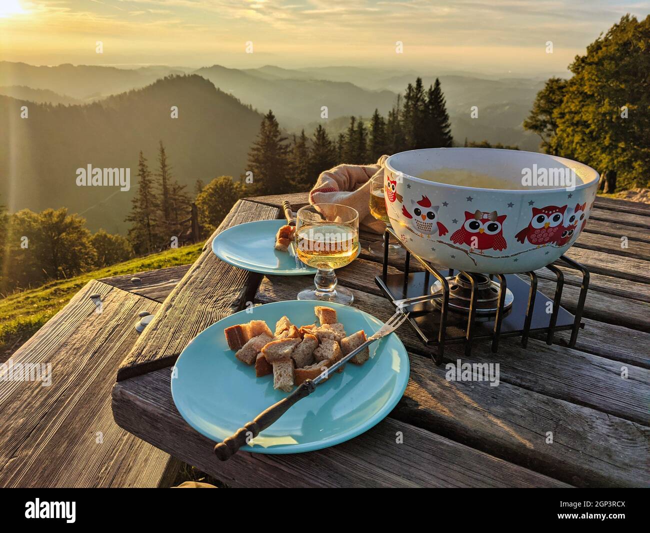 Fondue auf dem Schneelhorn. Traditionelle Schweizer Küche mit Käse bei Sonnenuntergang auf dem Hügel in Zürich. Abendessen mit Weißwein Stockfoto