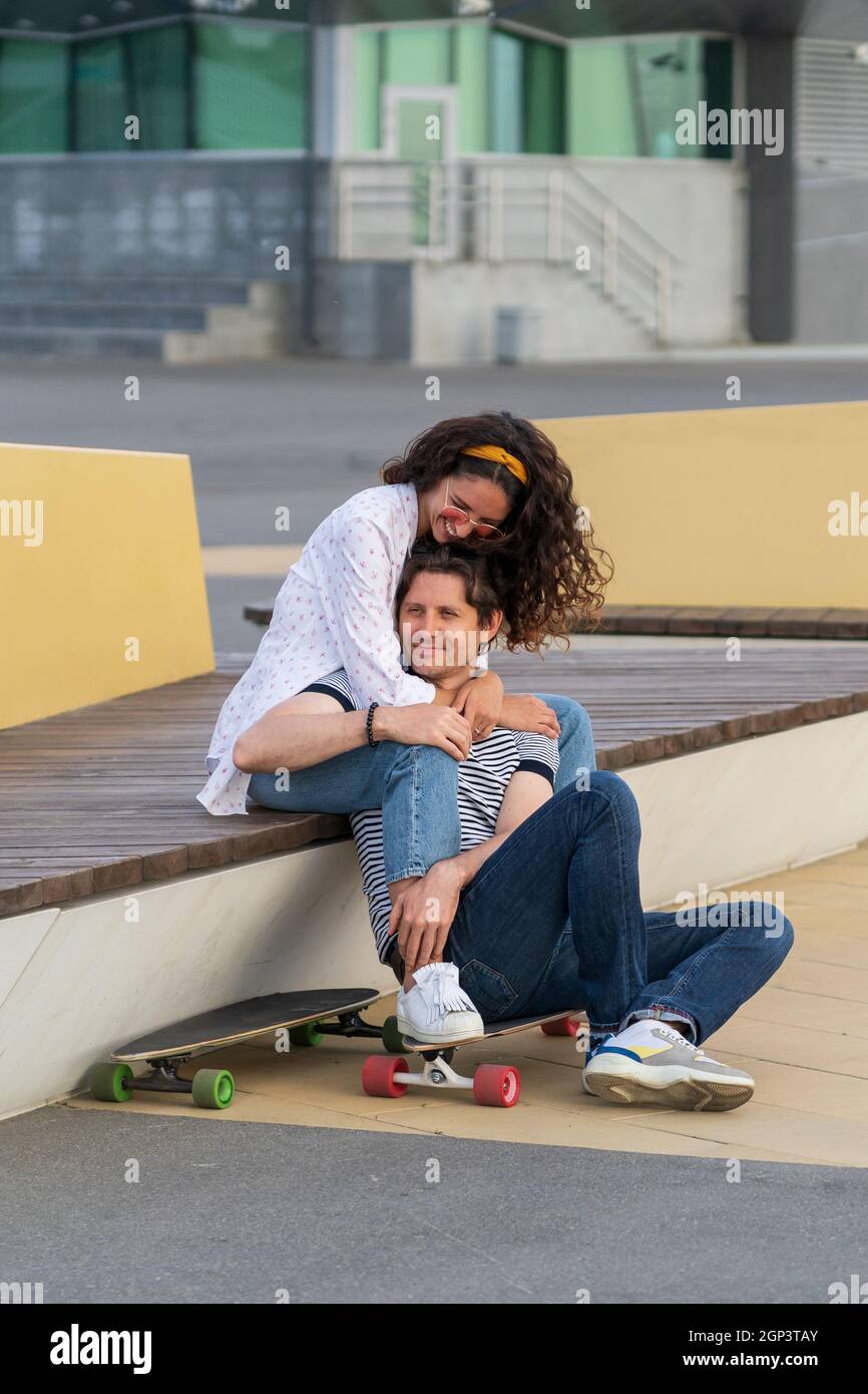 Ein junges verliebtes Paar genießt den Sonnenuntergang und umarmt sich auf Longboard. Trendige Männer und Frauen, die draußen chillen Stockfoto