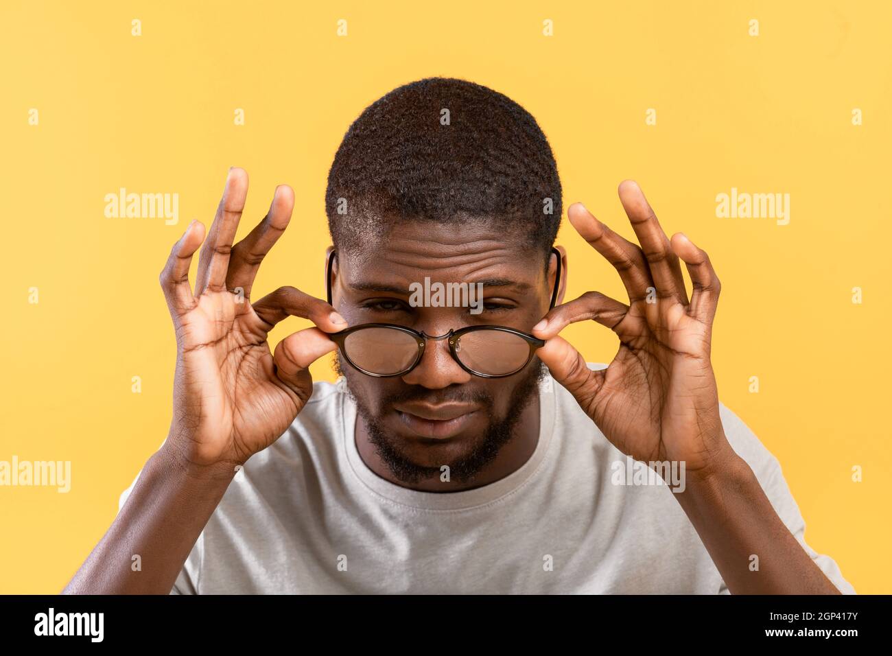 Schlechte Sehkraft. afroamerikanischer Kerl, der Augen zuckt und die Kamera anschaut, die Brille berührt, während er auf gelbem Hintergrund posiert. Vision Probleme Kontra Stockfoto