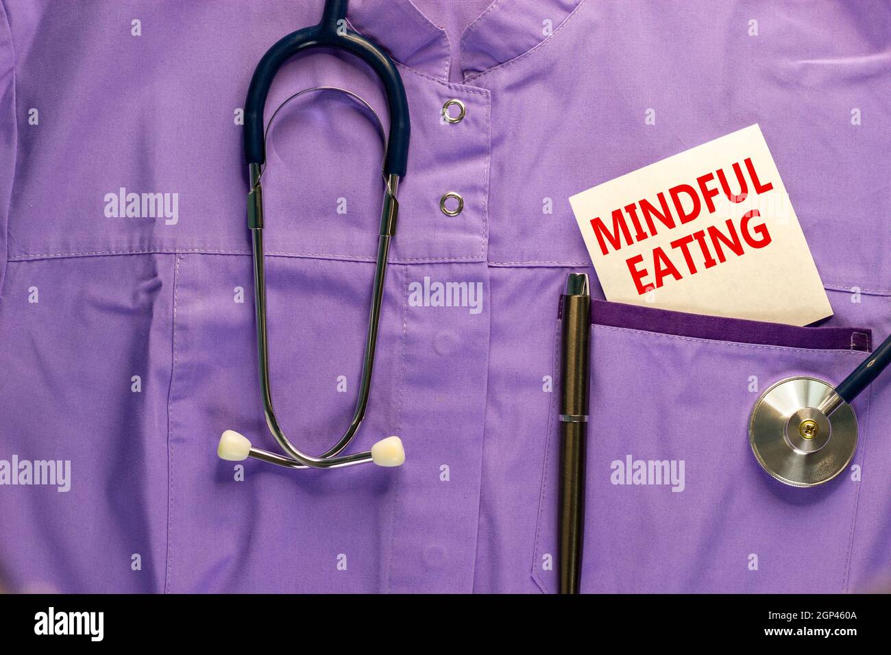 Symbol für „achtsames Essen“. Medizinische Uniform, weiße Karte mit Worten achtsames Essen, metallischer Stift und Stethoskop. Medizinisches und achtsames Esskonzept. Stockfoto